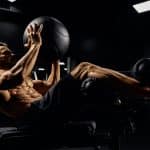 Side view of muscular caucasian man training abs with ball on bench in gym. Handsome young sportsman building core muscles, doing crunches in dark atmosphere. Concept of sport, fitness.